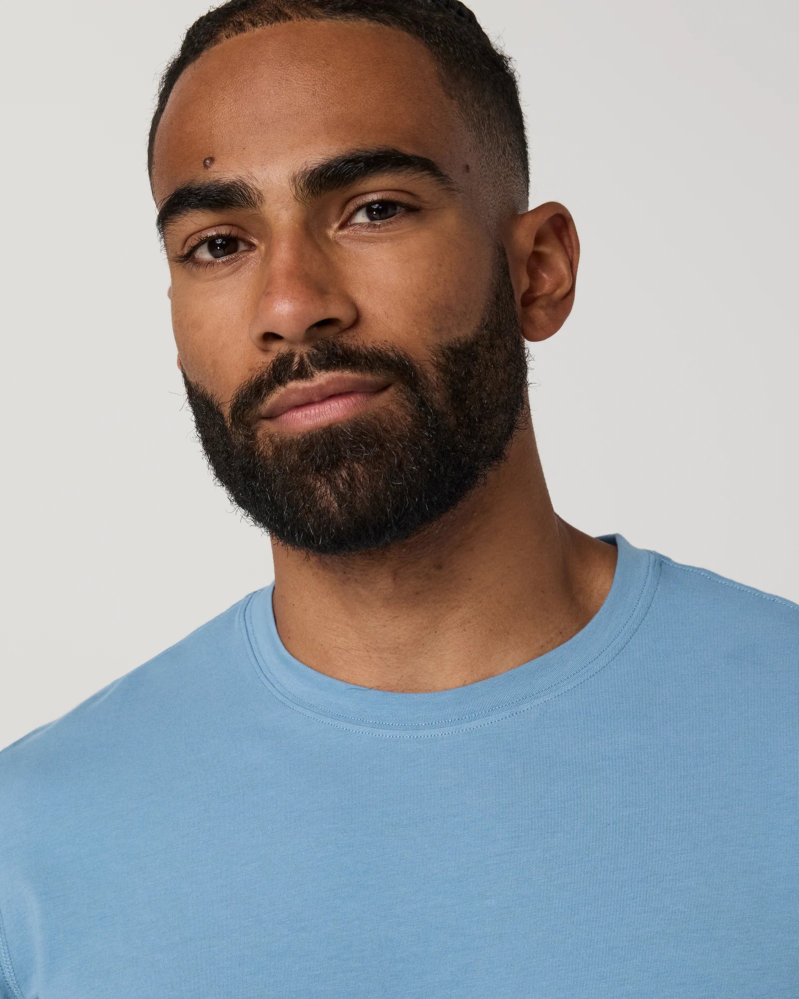 Man wearing a blue t-shirt and beige shorts on a plain background