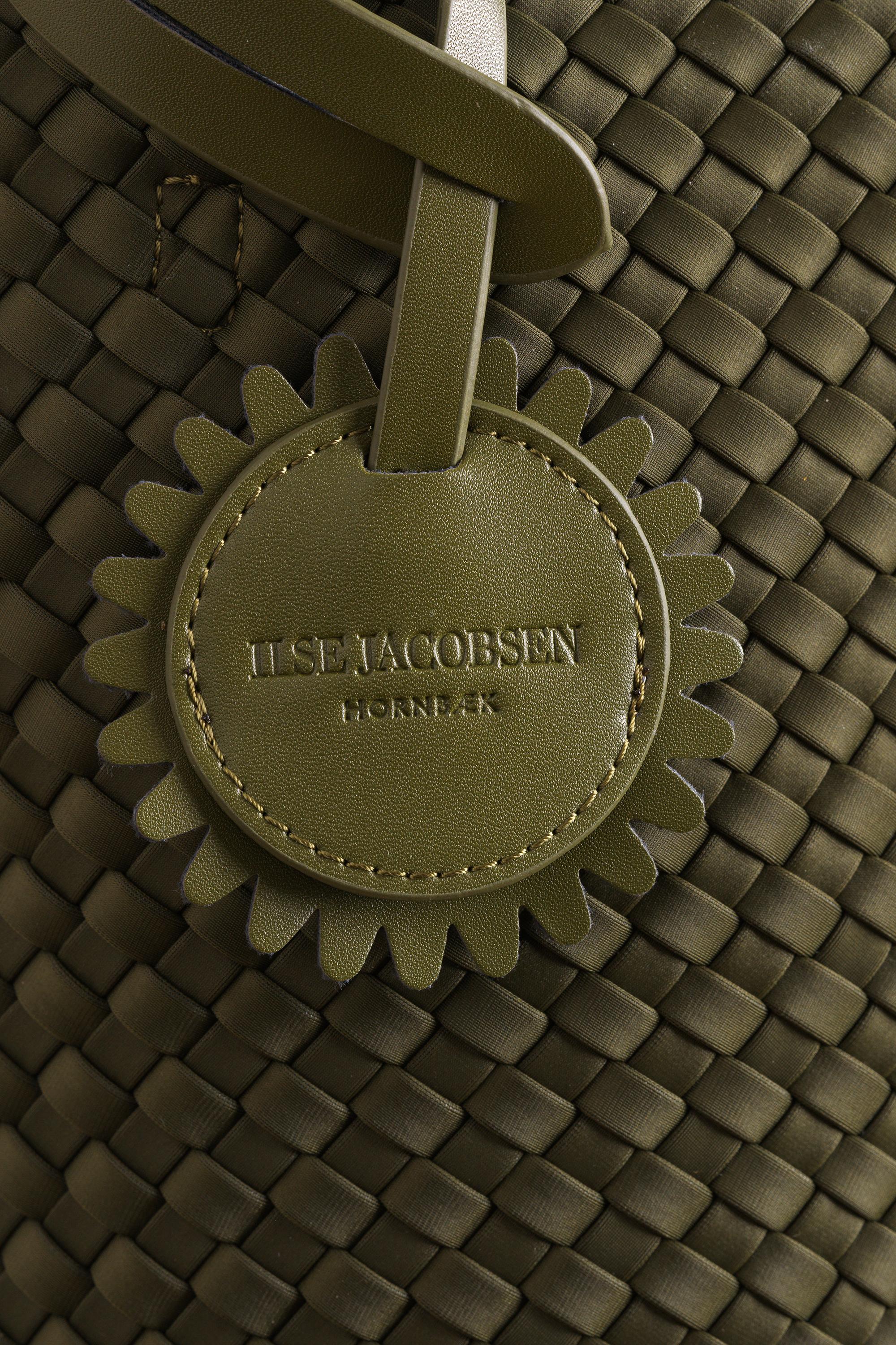 Close-up of an olive green woven leather bag with a circular embossed leather tag reading 'ILSE JACOBSSEN HORNBERG'.