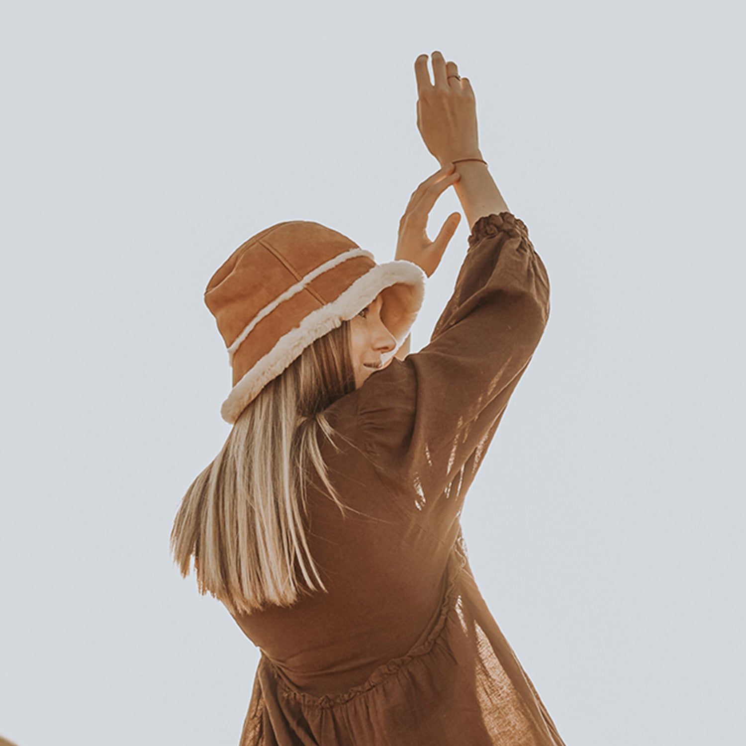 Person wearing a brown outfit and hat against a light blue background