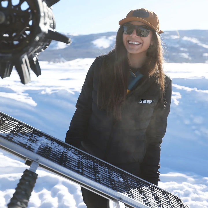 Person standing in the snow with a snowboard, wearing a black jacket and sunglasses.